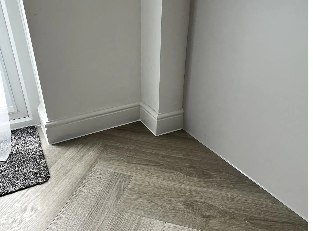 Skirting board sealed against herringbone flooring in a hallway