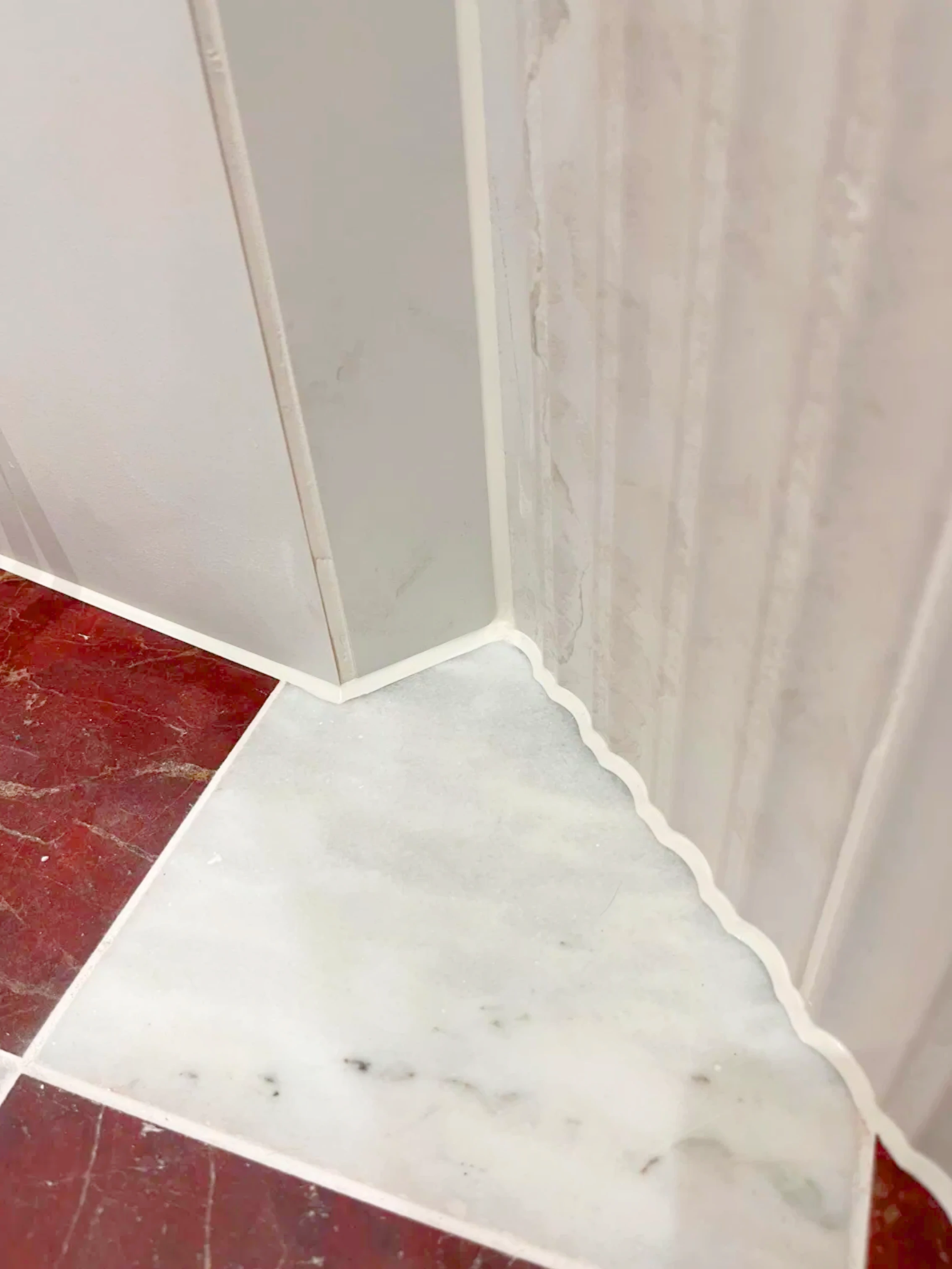 Close-up of a neat wavy sealant line where marble tile flooring meets a fluted tile wall corner, finished by Apex Sealants
