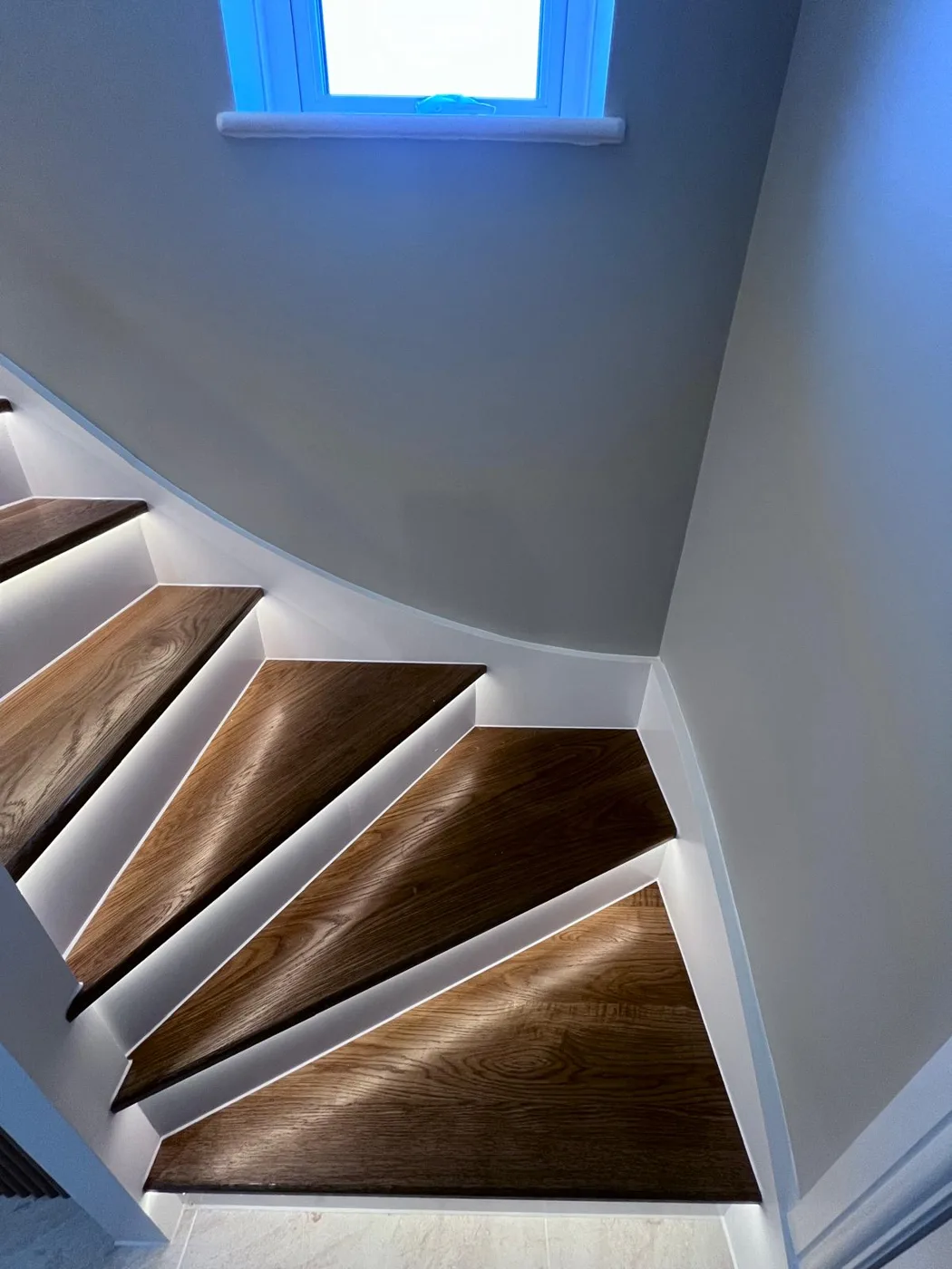 Oak staircase turn with white risers and LED strip lighting, clean sealant lines
